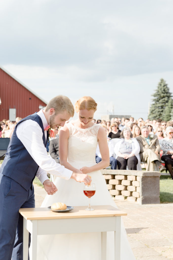 Bride and Groom break bread during communion at their ceremony at the Outpost Center in Chaska