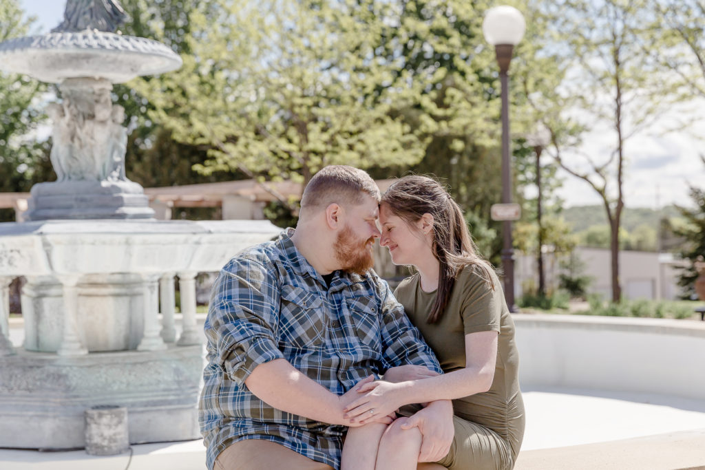a couple sit on a fountain during engagement session