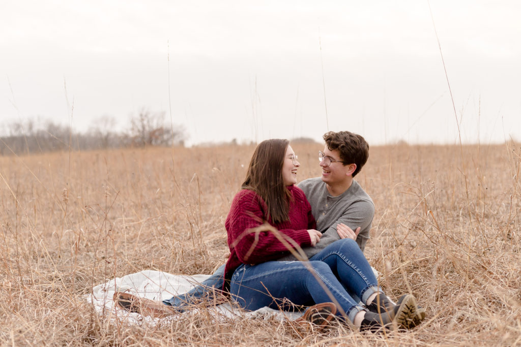 a couple sit in a field of tall grass during engagement session